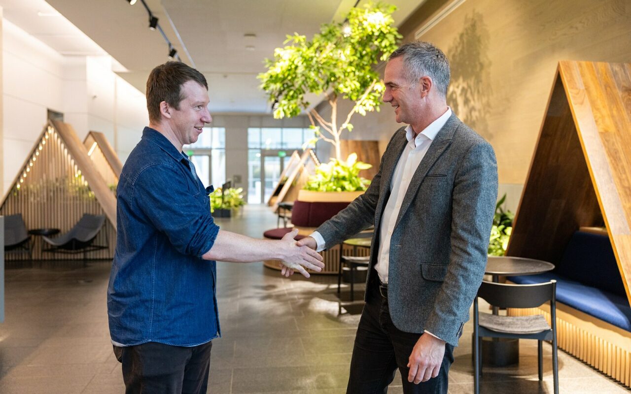 Deux hommes se serrent la main dans un espace de bureaux lumineux garni de plantes, lors d'une visite officielle chez Anthropic.