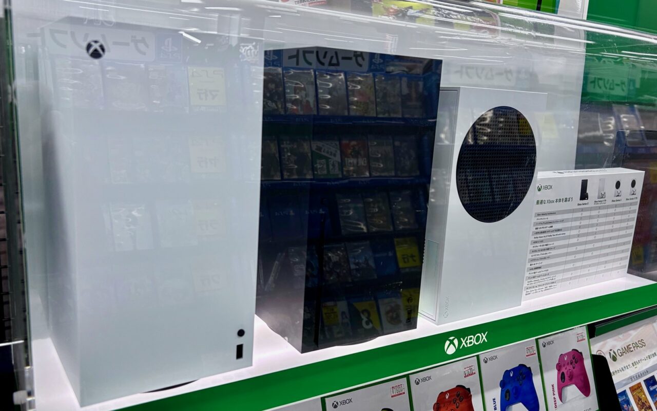 Consoles Xbox Series X et Series S blanches exposées dans une vitrine de magasin, au-dessus de manettes Xbox de couleur