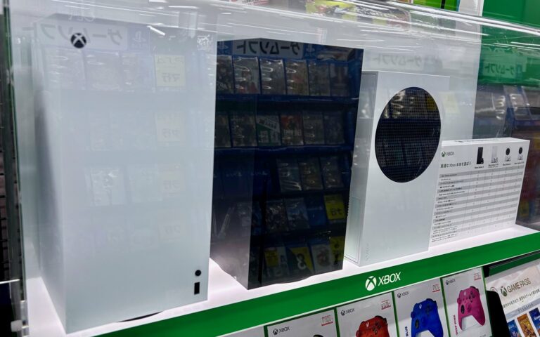 Consoles Xbox Series X et Series S blanches exposées dans une vitrine de magasin, au-dessus de manettes Xbox de couleur